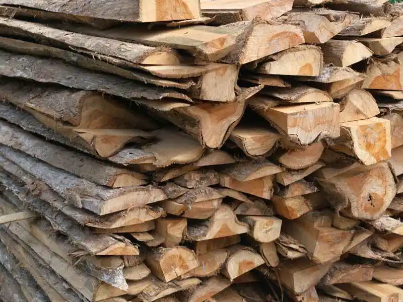 Raw timber residues and reclaimed teak wood waste stored at the factory for commercial 3D wood wall panels manufacturing.